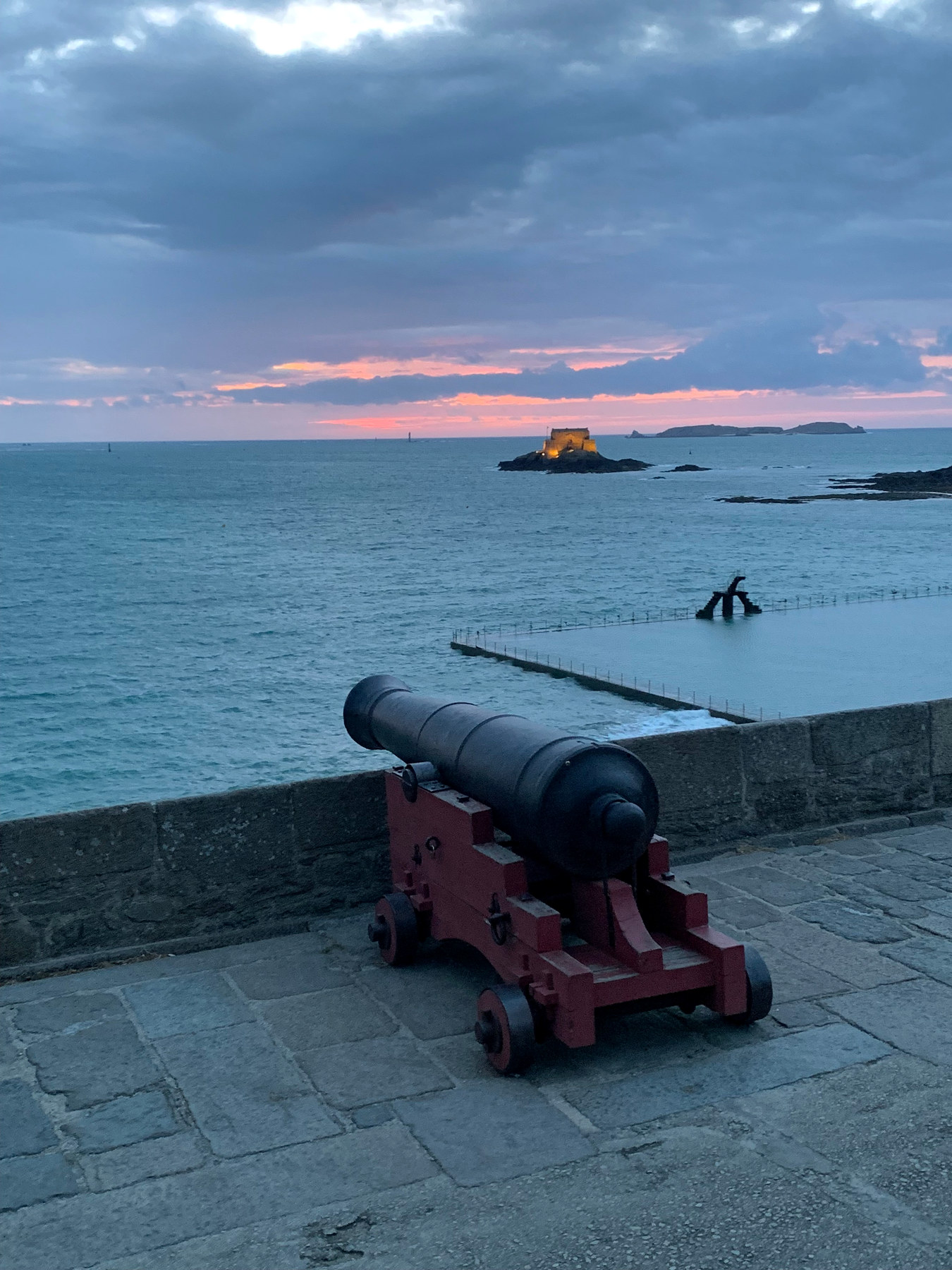 Un canon sur des remparts, une piscine d’eau de mer et un fort au coucher du soleil.