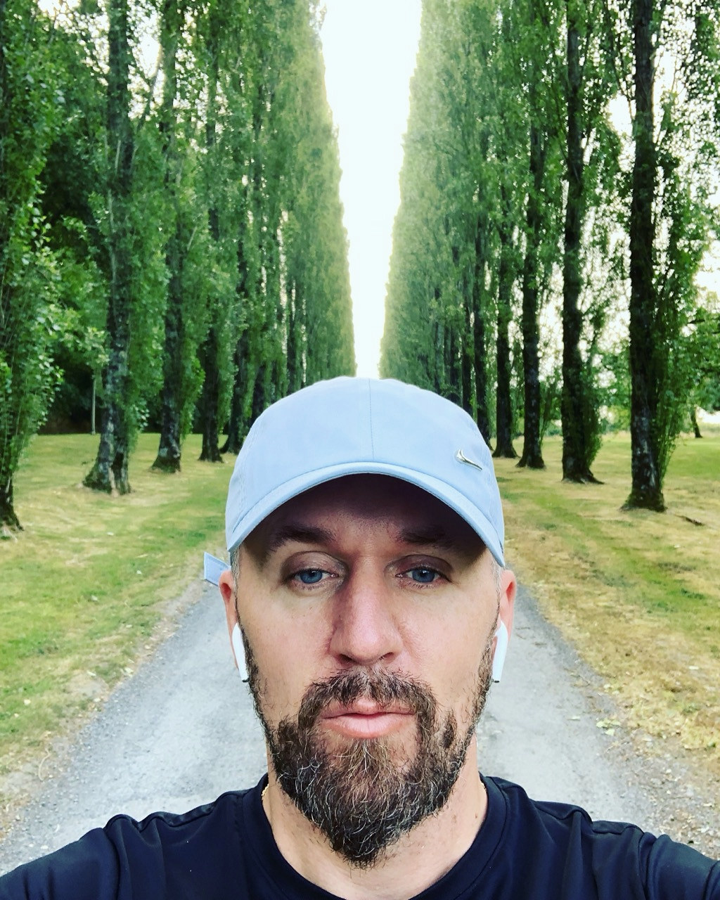 L’auteur en casquette bleue dans une allée bordée de grands arbres.