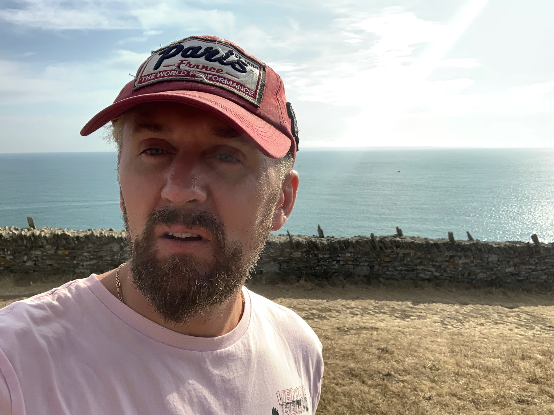 L’auteur en casquette rouge devant un muret et la mer.