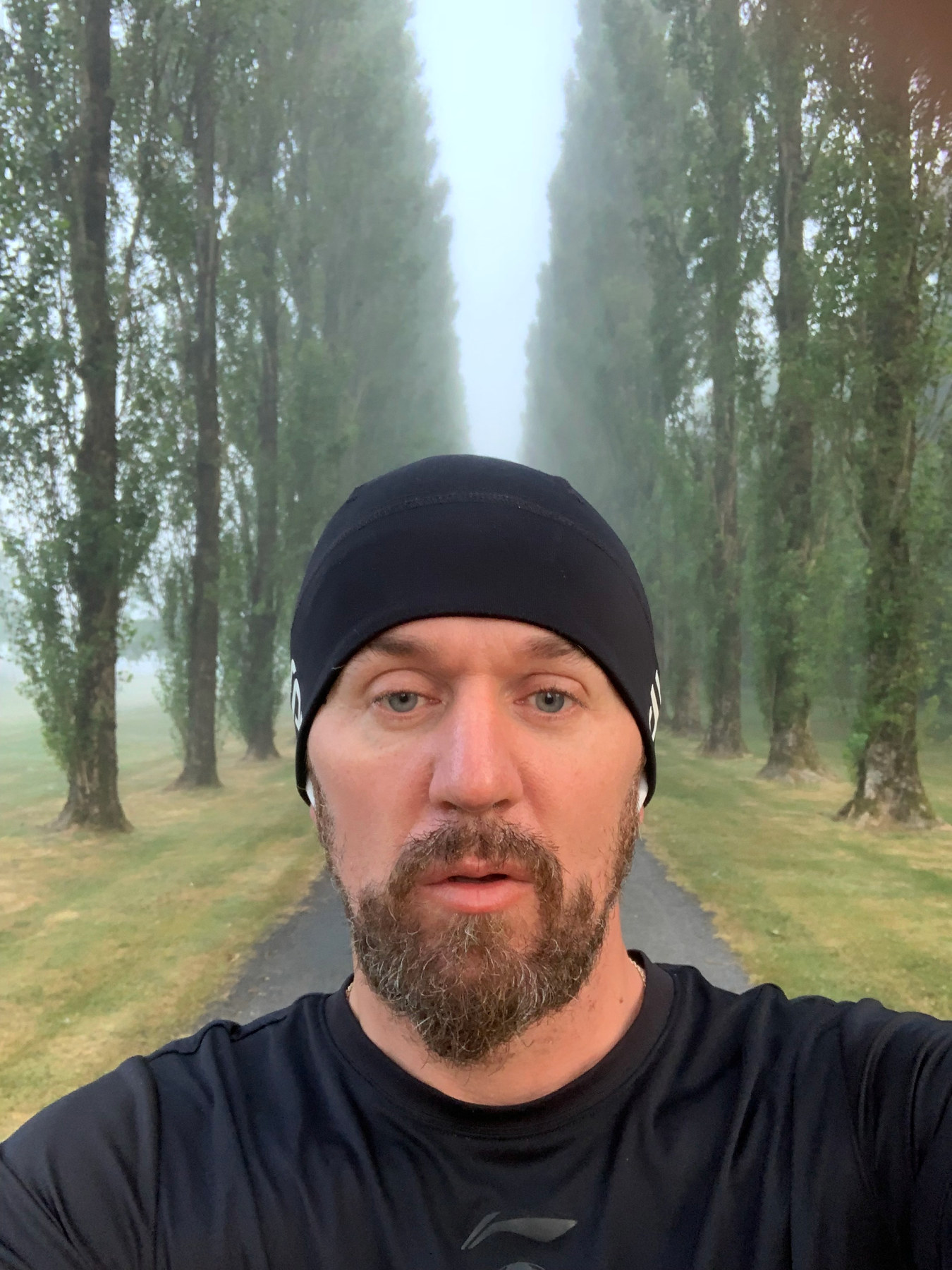 L’auteur en tenue de course et bonnet noir dans une allée d’arbres brumeuse.