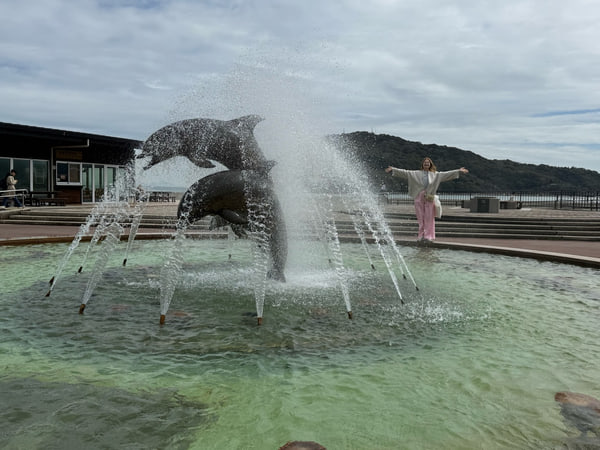 イルカの噴水のそばで両手を広げる女性
