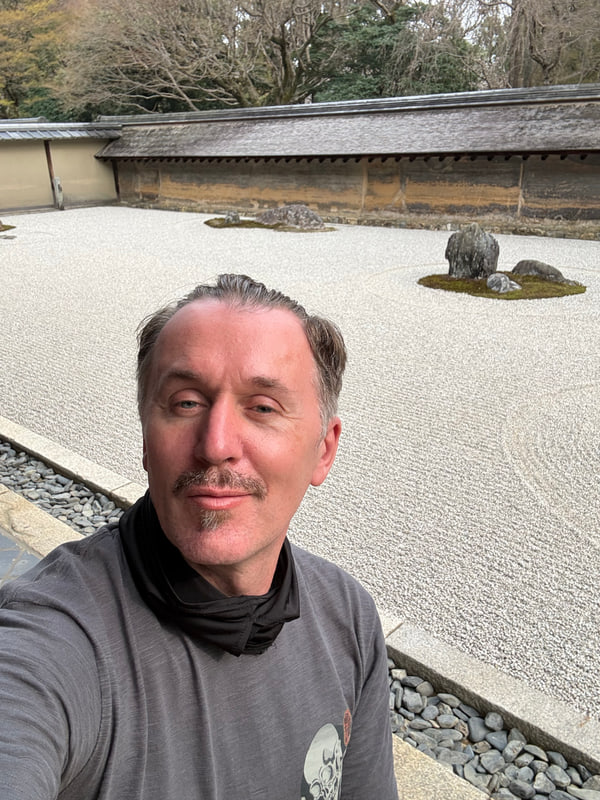 白砂と石が並ぶ石庭を背景にした男性の自撮り写真