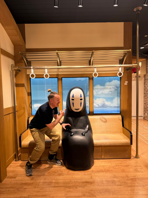 電車の座席を再現した展示で、カオナシの隣でポーズをとる男性