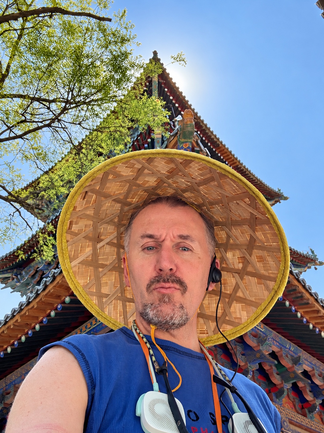 戴着草帽，身后是树枝与建筑屋檐。